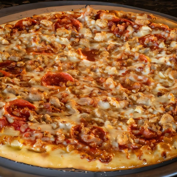Close-up of a Task Force Pizza with melted cheese, pepperoni, and chicken on a dark pan.
