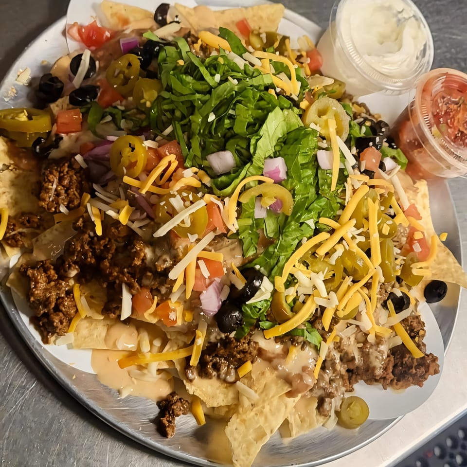 A large platter of nachos with ground beef, cheese, lettuce, tomatoes, olives, and jalapeños.