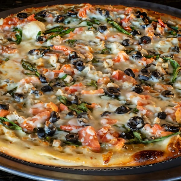 A Task Force Pizza with melted cheese, black olives, diced tomatoes, and green herbs.