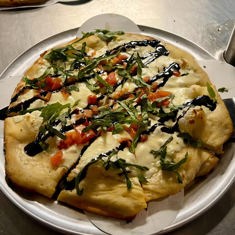 Task Force Pizza's white pizza with tomatoes, basil, and balsamic glaze on a metal tray.