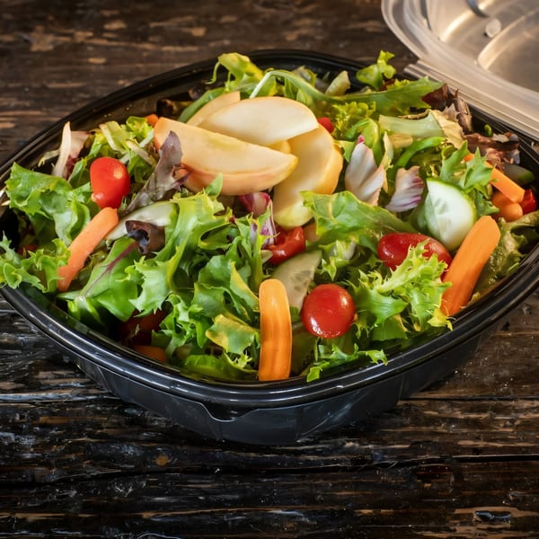 Fresh garden salad with mixed greens, cherry tomatoes, carrots, cucumbers, and apple slices in a black container.